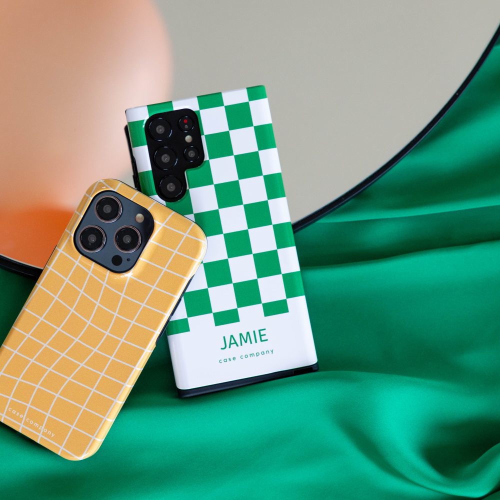 Duas capas resistentes: uma amarela em xadrez para iPhone e uma verde aos quadrados com o nome Jamie